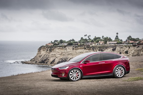 A red Tesla Model X SUV parked on a waterfront.