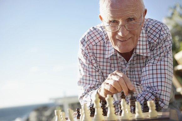 A retired man playing chess on the beach.