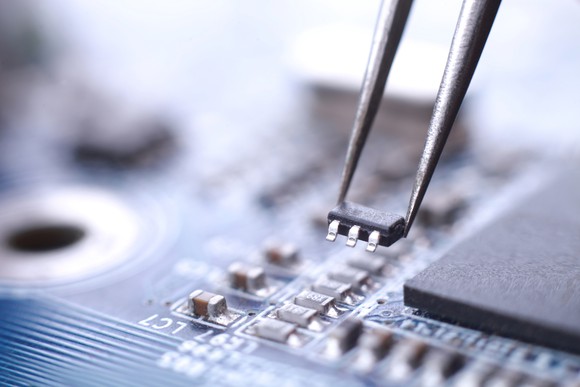 A technician installs a microchip with tweezers.