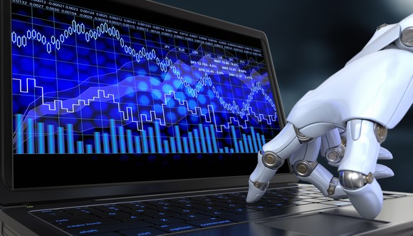 A robotic hand points to stock charts on a computer screen.