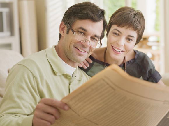 A middle-class couple looking for stocks to buy in a financial newspaper.