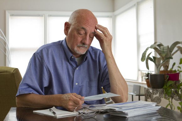 Senior man looking worried, staring at a stack of paperwork.