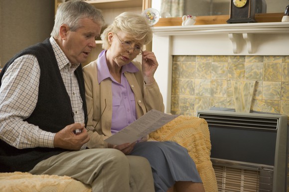 Senior couple, sitting on a sofa, reading a document.