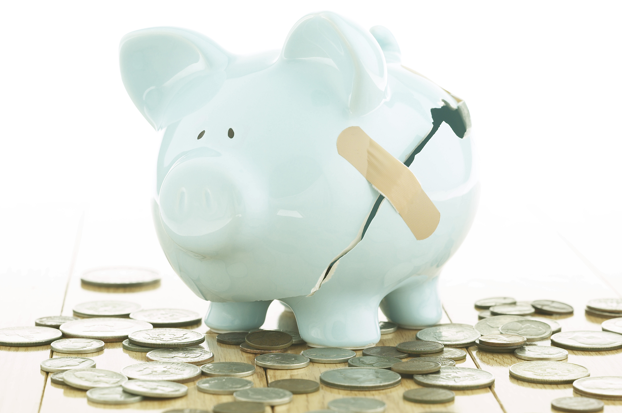 A blue piggy bank has a bandage over a large crack on its side, with coins spilled out beneath it.