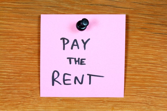 A pink sticky note reading "pay the rent" is tacked to a wooden surface.