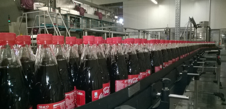 Coke bottles coming down the line in a bottling plant.