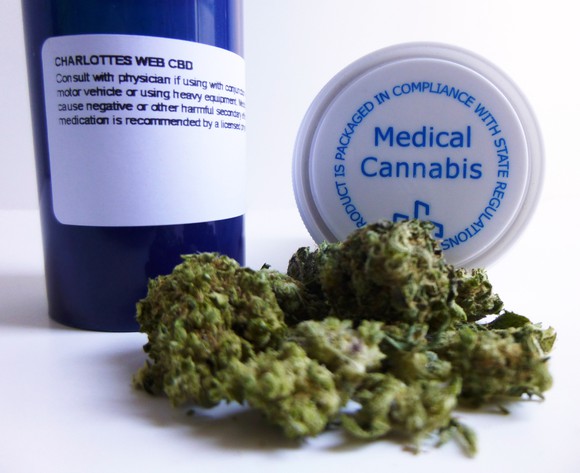 Marijuana buds lie in front of a blue prescription bottle and a bottle cap that reads "medical cannabis."