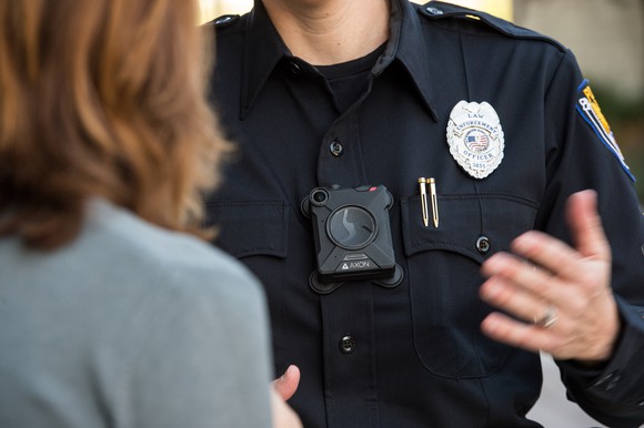 Police officer wearing an Axon body camera while talking to a civilian.
