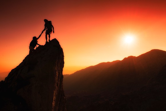 Two mountain climbers reaching the summit at sunset.