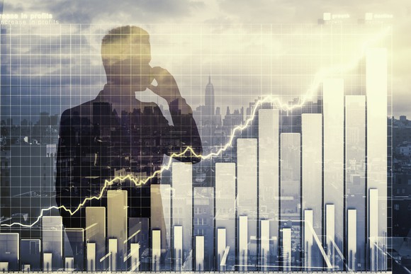 A businessman talks by phone, with a city skyline behind him. In front of him is an overlay of a rising stock chart.