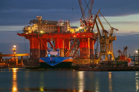 An offshore rig in a dockyard at night, with a waterway in the foreground.