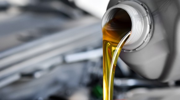 A container of motor oil being poured out into a car engine.