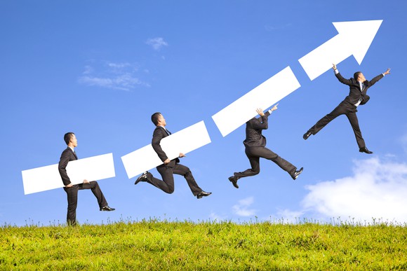 Businessmen hold on to a stock chart rising into the sky.
