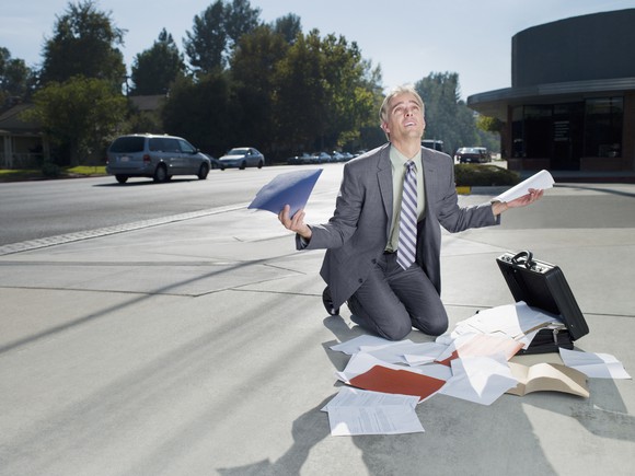 Frustrated businessman kneeling over a heap of unsorted papers.