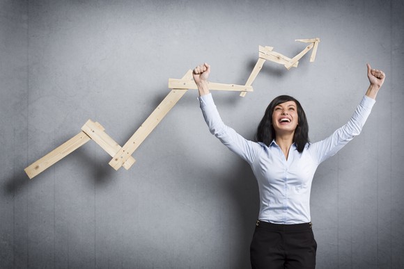 A happy woman standing in front of a rising stock chart. 