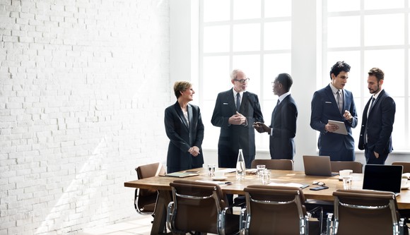 Executives standing around a boardroom table talking.