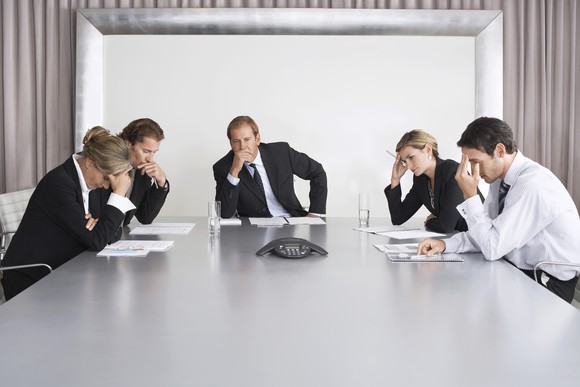 Business people sitting around a table, looking concerned.