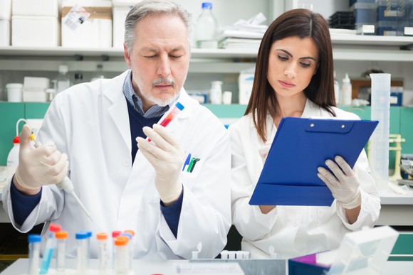 Biotech lab techs examining a test tube and taking notes.