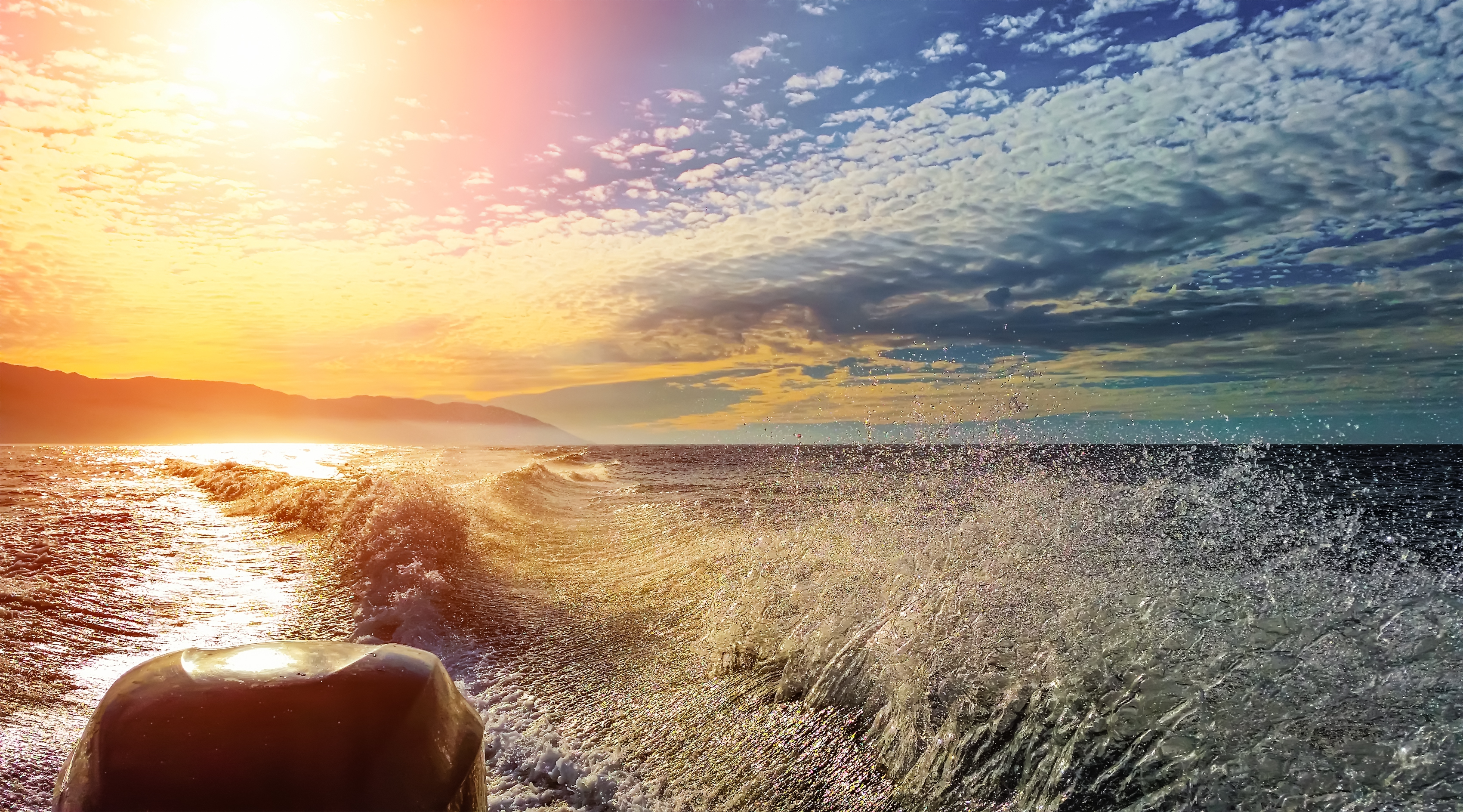 A view from a speedboat with the sun reflecting on the water.