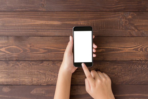 Hands holding smartphone against wooden backdrop