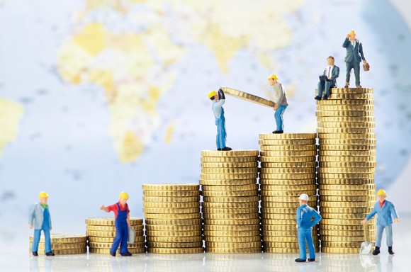 Toy construction workers and businessmen building successively taller piles of coins.