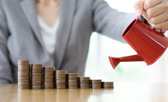 A woman holds a watering can over stacks of coins.