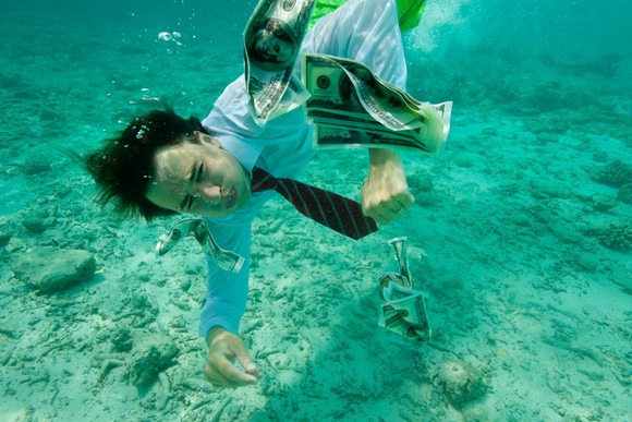 A business man swimming underwater collects money.