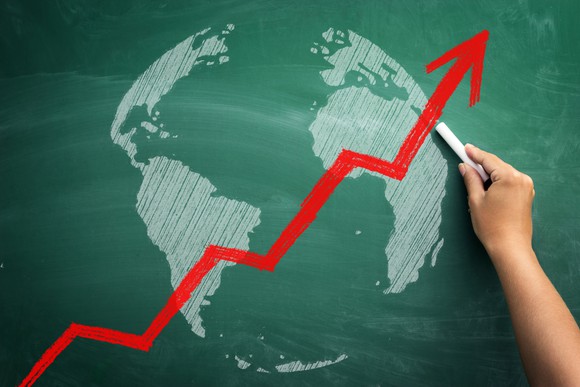 A hand holding a piece of chalk sketches the continents of the globe, with a red upward-pointing arrow in the foreground.