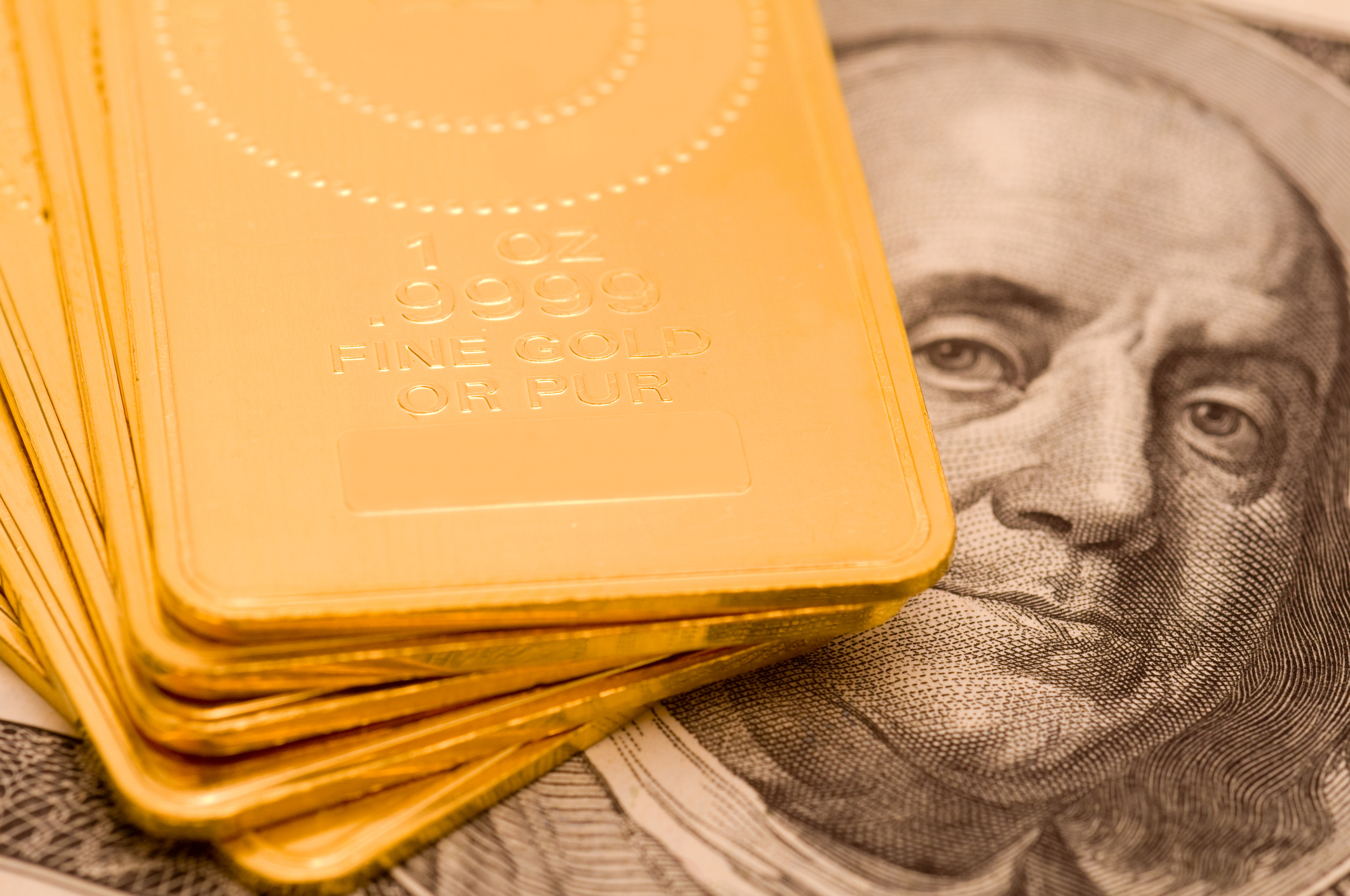 Gold ingots lying atop a hundred dollar bill.
