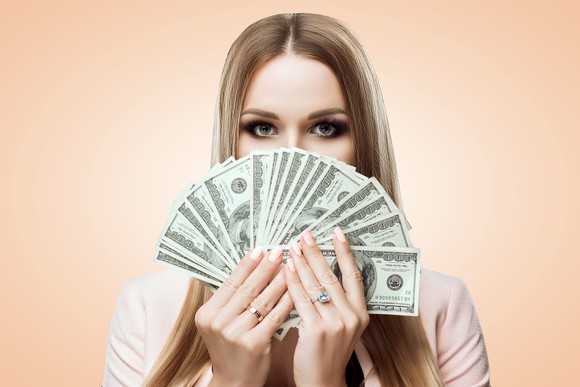 A woman holding money in front of her face.