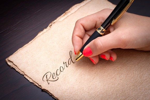 Woman writing "Record" on a sheet of papyrus.