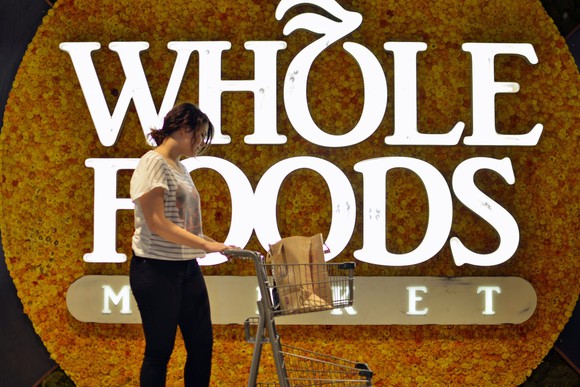 A woman pushing a shopping cart in front of a "Whole Foods" sign
