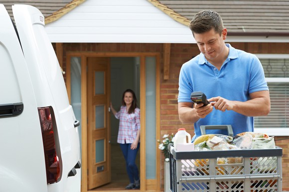 A man delivers an online order of groceries, while the recipient waits at her door.