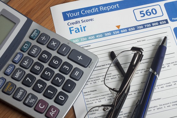 A credit report, with a score of 560, sits on a table with a pen, glasses, and calculator.