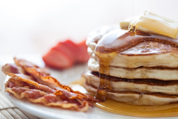 A stack of pancakes with a side of bacon and strawberries.