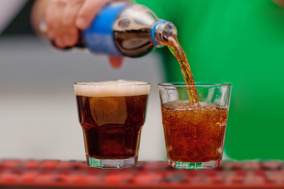 Person pouring soda into a glass.