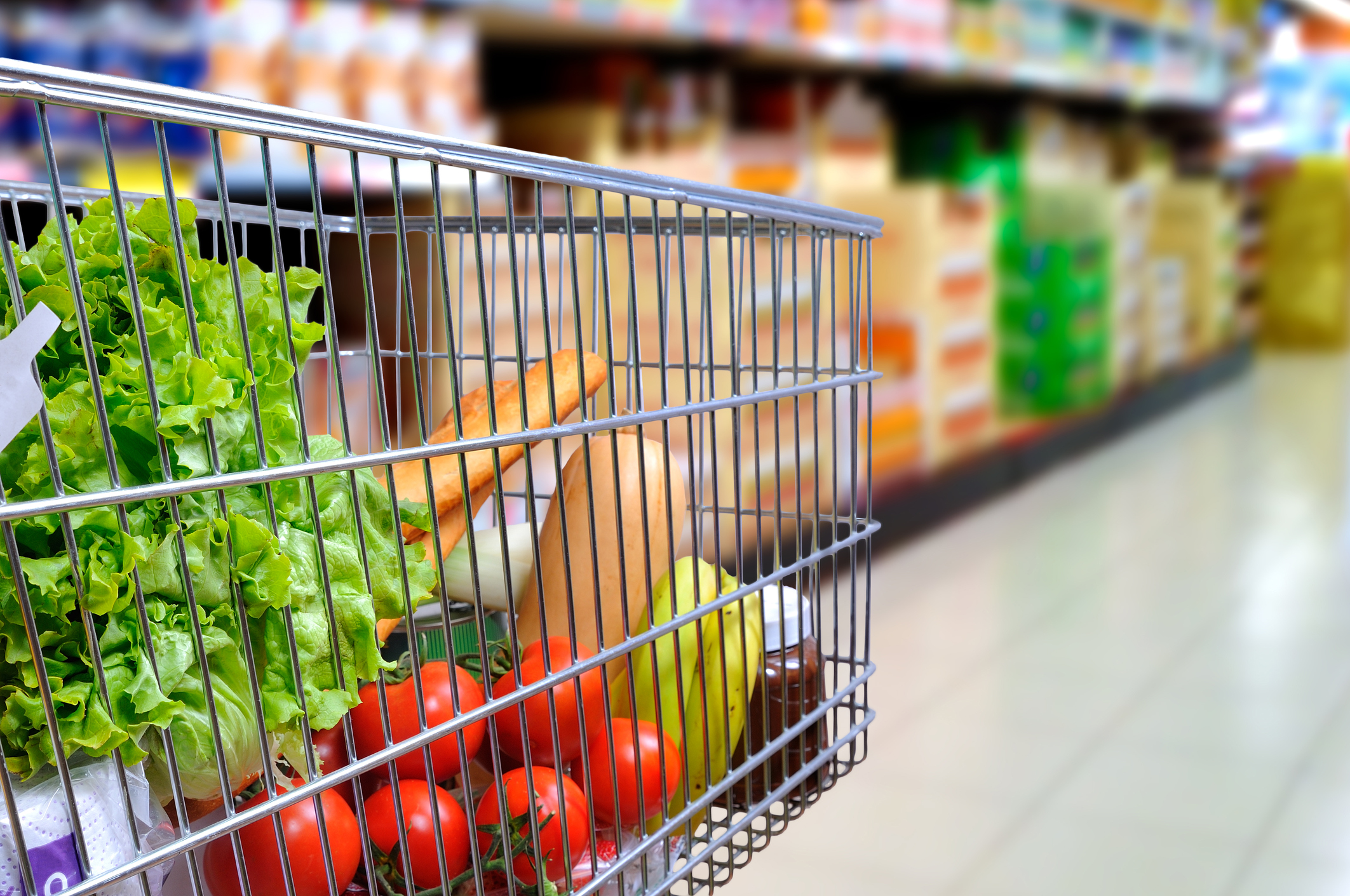 A shopping cart full of produce in a supermarket.