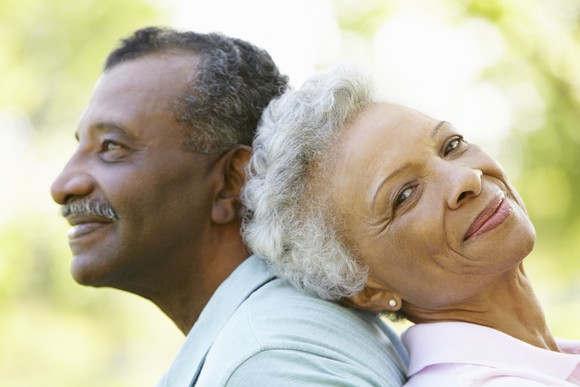 Senior couple sitting back to back and smiling