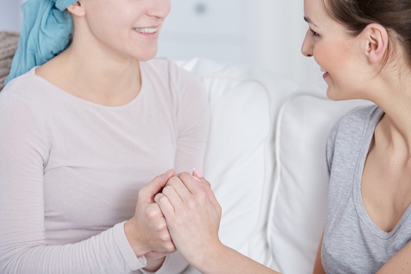 A cancer patient holds hands with a friend.