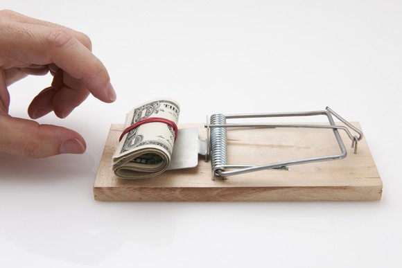 A hand reaches toward money on a mousetrap.