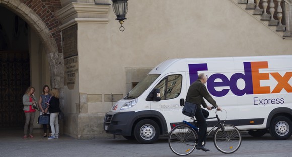 FedEx Express truck parked near a university alcove with students and bicyclist in frame.