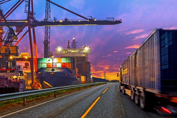 Freight truck driving beside container docks near dusk.