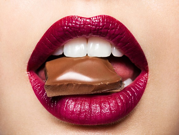 Piece of milk chocolate in woman's mouth.
