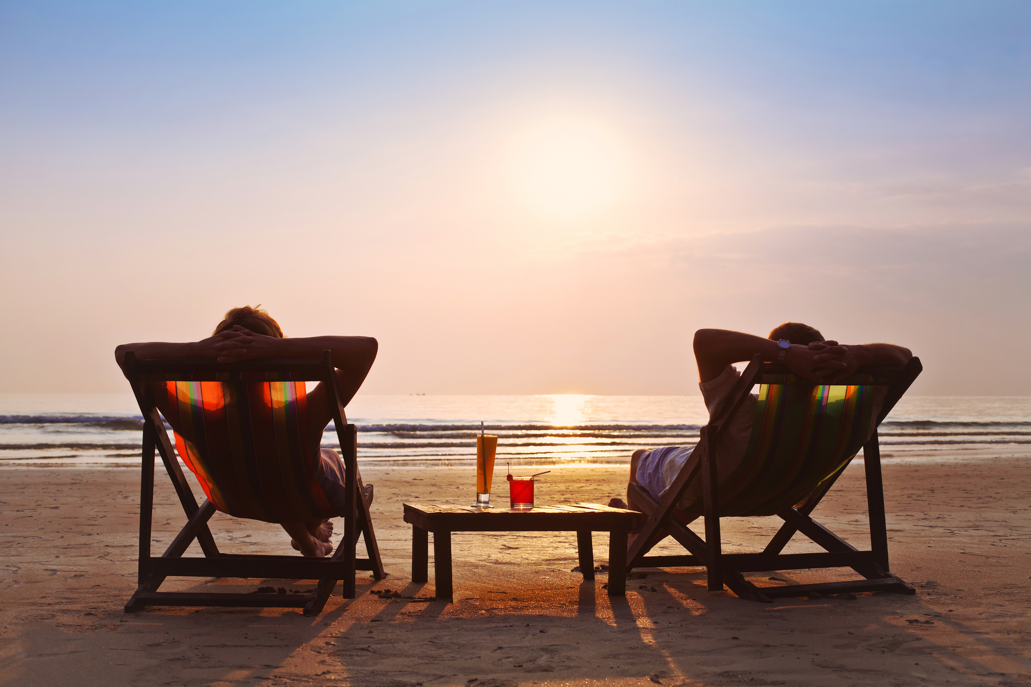 Two people on beach chairs at beach as sun sets