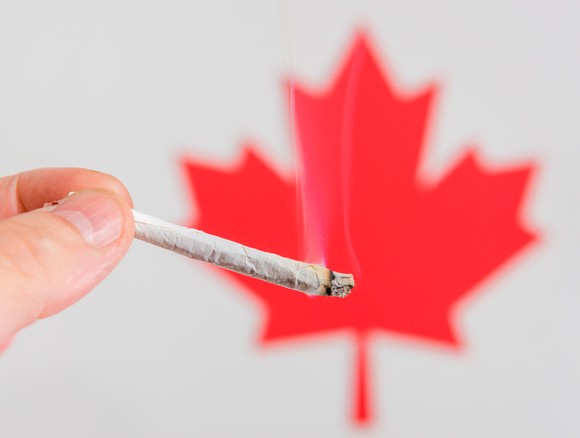 A person holding a cannabis joint in front of Canada's maple leaf.