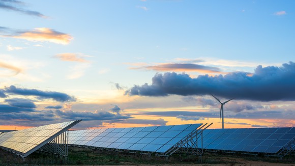 A solar array with one wind turbine in the background. 