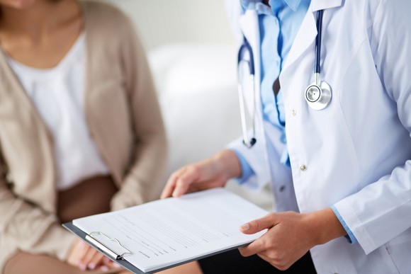A doctor holding a clipboard in front of a patient.