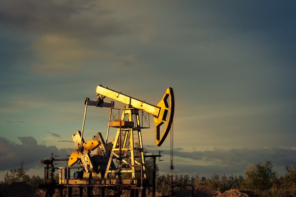 An oil pump jack against a background of sky at sunset.