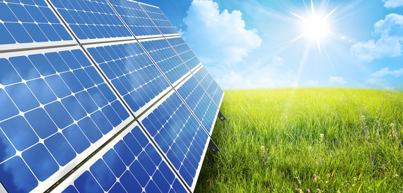 Solar panels in a field with the sun in the background.