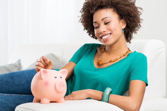 A young woman putting money into a piggy bank.